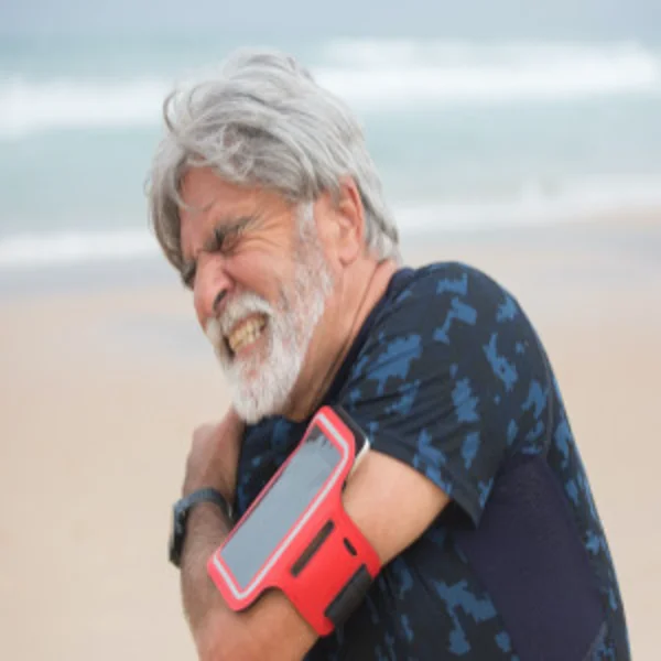 Hombre mayor se sujeta el hombro adolorido mientras camina en la playa