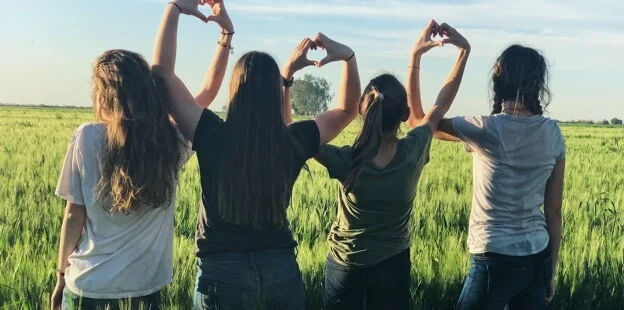 Grupo de voluntarias formando corazones con las manos en un campo